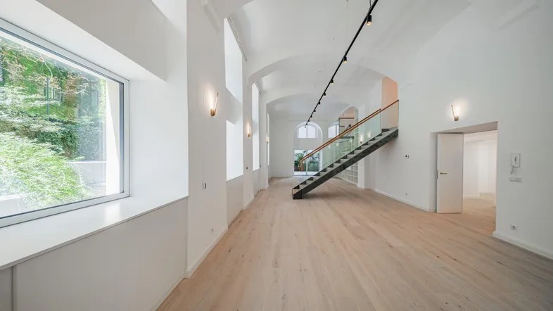 Offener Wohnbereich mit hohen Gewölbedecken, großen Fenstern und moderner Treppenkonstruktion.