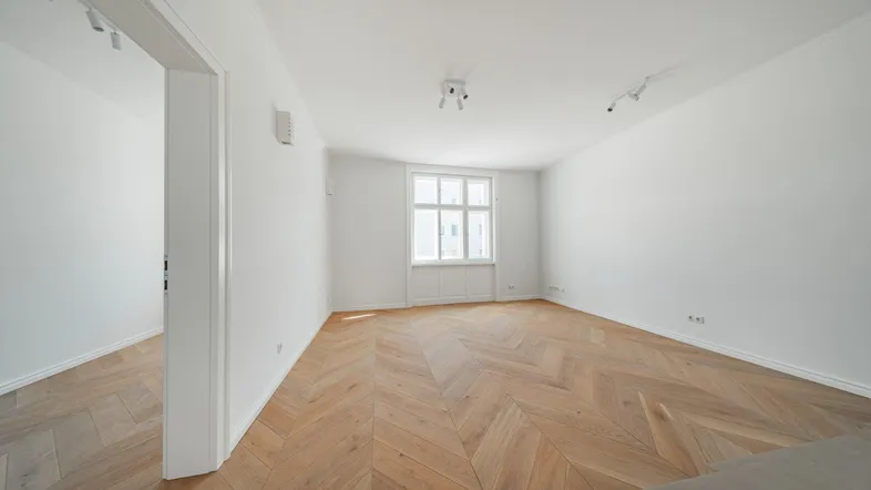 Helles, leeres Zimmer mit Fischgrätparkett und weißen Wänden, bereit zur individuellen Gestaltung.