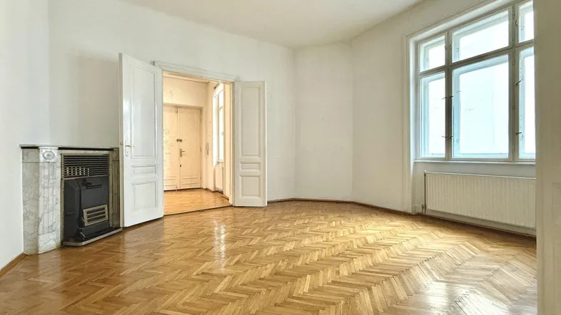 Helles Wohnzimmer mit Fischgrätparkett, hohen Fenstern und einem traditionellen Ofen.