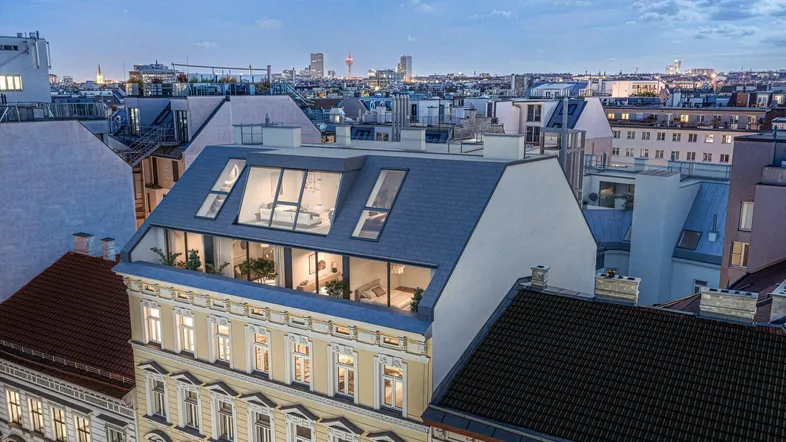 Abendliche Luftaufnahme eines Gebäudes mit modernem Dachausbau und Stadtblick.
