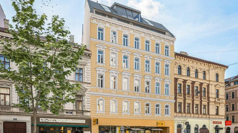 Historisches Gebäude mit modernem Dachausbau und Geschäften im Erdgeschoss an einer Stadtstraße.
