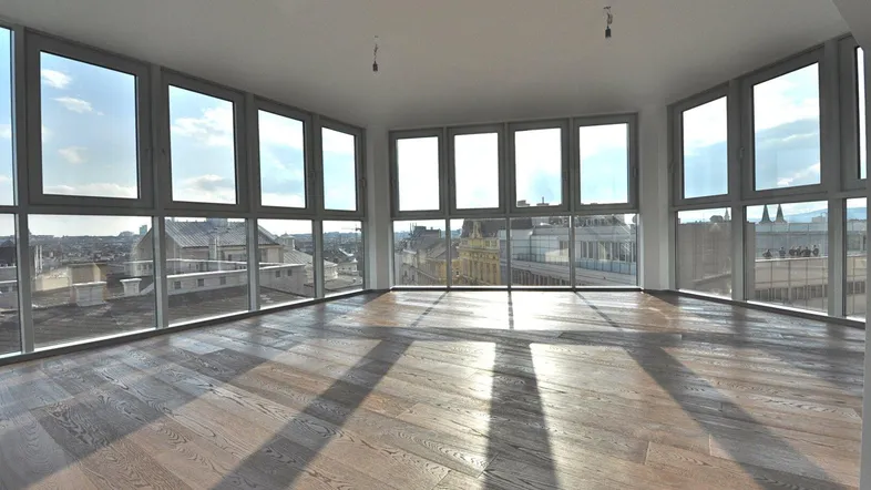 Helles, leeres Zimmer mit großen Fenstern und Holzboden, bietet einen weiten Stadtblick.