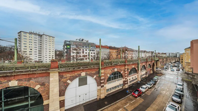 Blick auf die belebte Straße mit historischem Viadukt und umliegenden Gebäuden unter blauem Himmel.