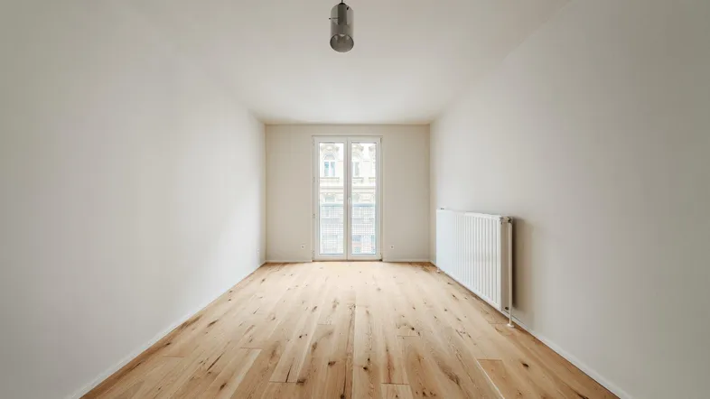 Helles, leeres Zimmer mit neuem Holzfußboden und Fenster zur Straße, bereit zur Einrichtung.