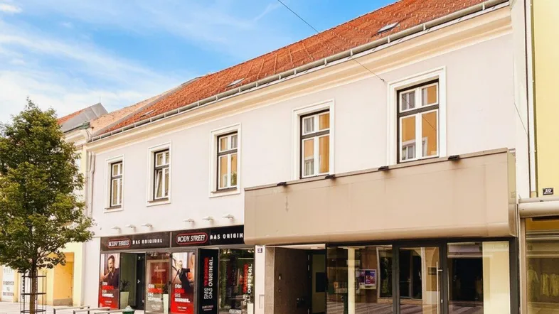 Modernes Gebäude mit großen Schaufenstern und rotem Ziegeldach in einer Stadtstraße.
