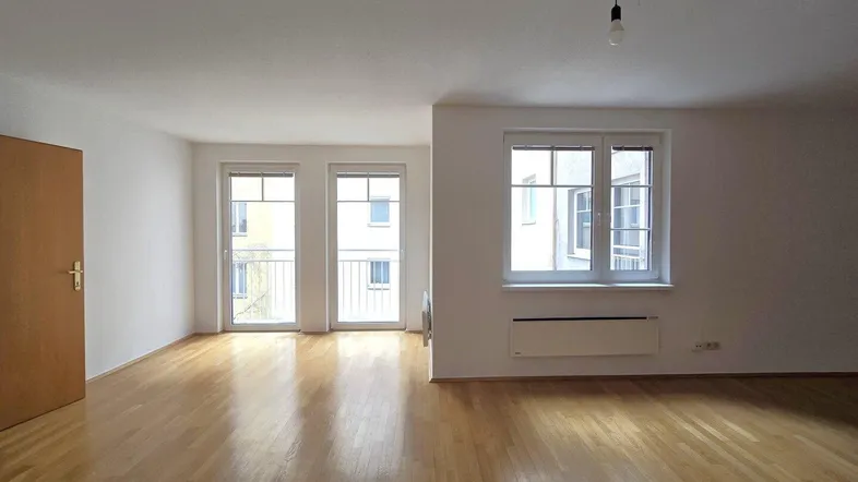 Helles Wohnzimmer mit Parkettboden, weißen Wänden und Zugang zu französischen Balkonen.
