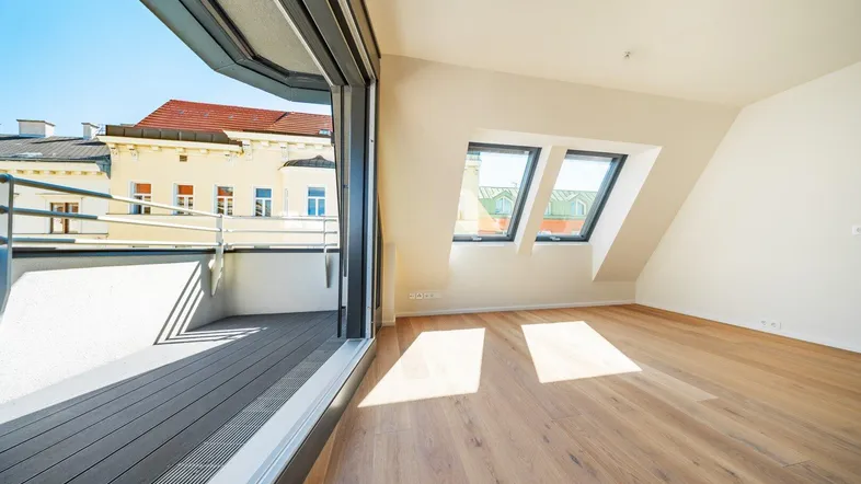 Heller Raum im Dachgeschoss mit Holzboden, großen Schiebetüren zur Terrasse und Dachfenstern.