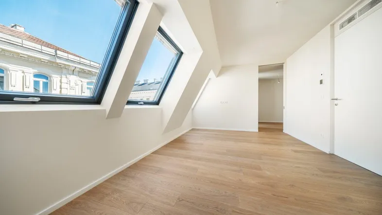 Helles Zimmer im Dachgeschoss mit Holzboden, schrägen Wänden und großen Dachfenstern.