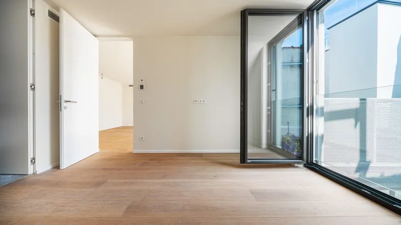 Helles, leeres Zimmer mit Holzboden und Zugang zu einem Balkon, ideal für modernes Wohnen.