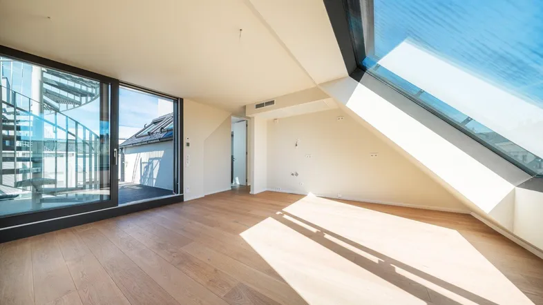 Heller Wohnraum im Dachgeschoss mit großen Dachfenstern, Holzboden und Zugang zur Wendeltreppe.
