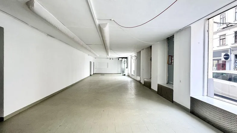 Langer, leerer Geschäftsraum mit großen Schaufenstern zur Straße und hellen Wänden, bereit zur Gestaltung.