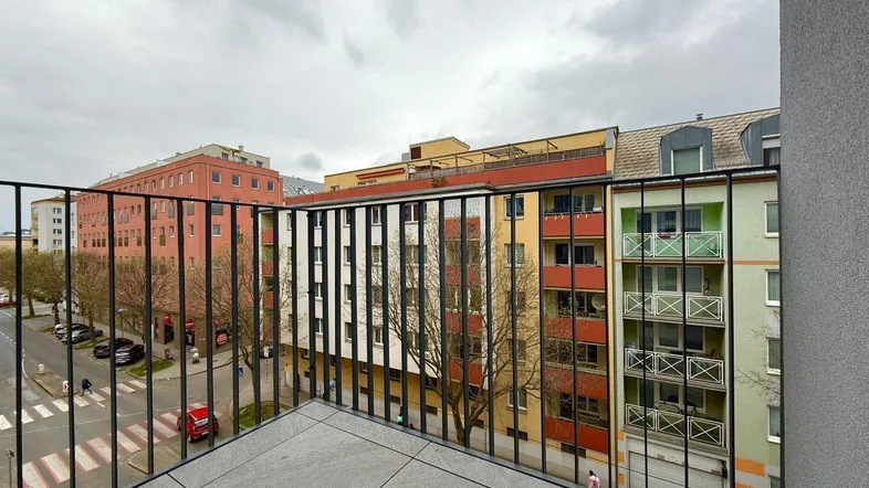 Geräumiger Balkon mit Fliesenboden und Blick auf die umliegenden Gebäude und die Straße.