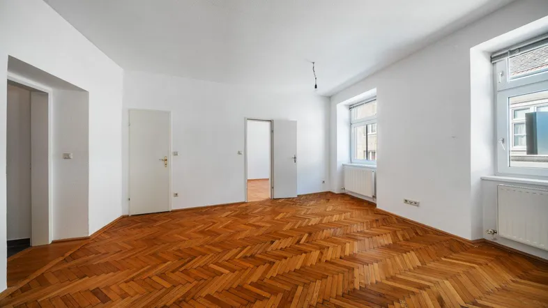 Helles Zimmer mit Fischgrätparkettboden und zwei Fenstern, bereit zur individuellen Gestaltung.