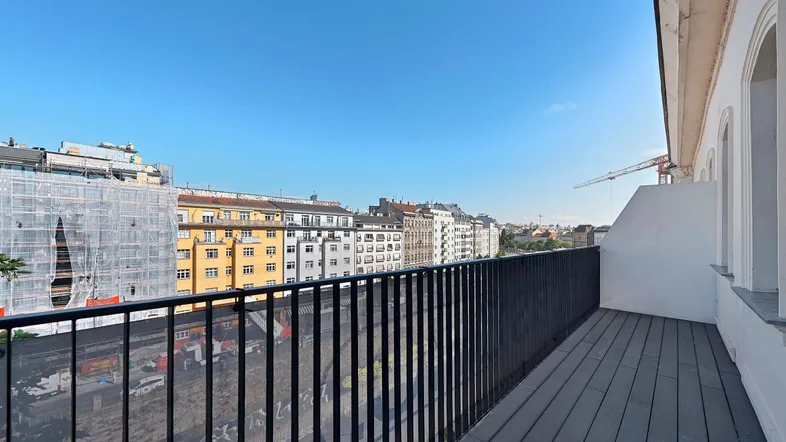 Geräumiger Balkon mit Holzboden und weitem Blick über die Stadt und umliegende Gebäude.