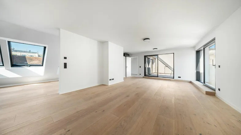 Heller, leerer Raum mit Holzboden, großen Fenstern und Zugang zu einem Außenbereich.