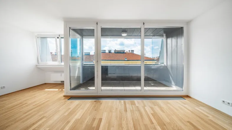 Helles Zimmer mit Holzboden und Zugang zu einem verglasten Balkon mit Stadtblick.