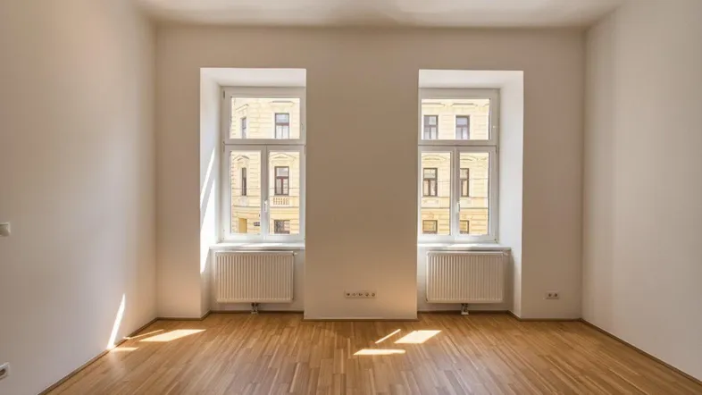 Helles, leeres Zimmer mit Parkettboden und zwei großen Fenstern, die viel Tageslicht hereinlassen.