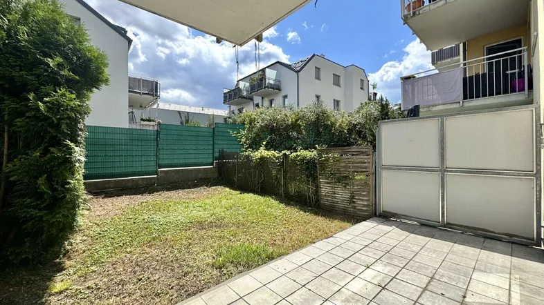 Gepflasterte Terrasse mit angrenzendem Rasenbereich und Blick auf umliegende Gebäude.