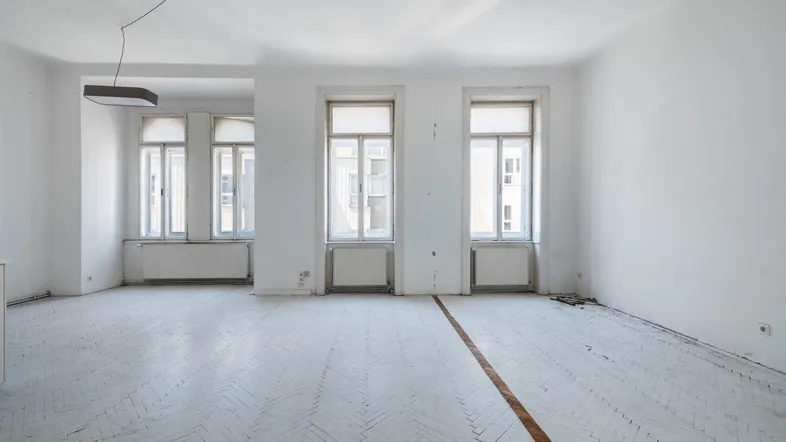Helles, leeres Zimmer mit Fischgrätparkett und hohen Fenstern, bereit zur individuellen Gestaltung.
