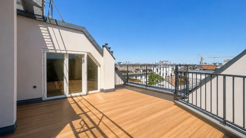Geräumige Dachterrasse mit Holzboden und weitem Blick über die Stadt unter blauem Himmel.