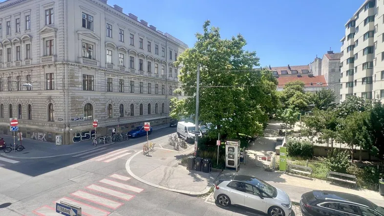 Blick auf die belebte Straßenkreuzung mit umliegenden Gebäuden und Grünflächen unter blauem Himmel.