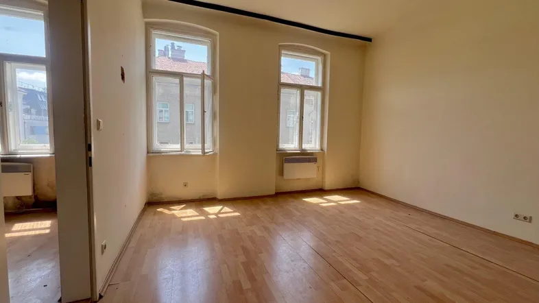 Heller Raum mit Holzfußboden und zwei Fenstern, bereit für eine Renovierung.