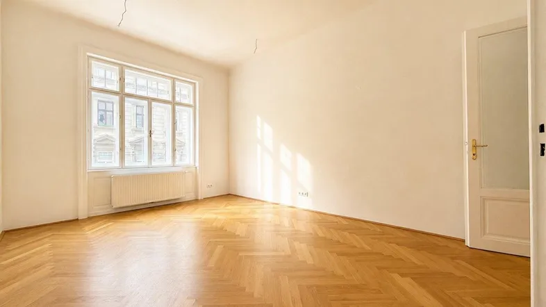 Helles Zimmer mit Fischgrätparkett, hohen Fenstern und viel Tageslicht, ideal als Wohnzimmer.