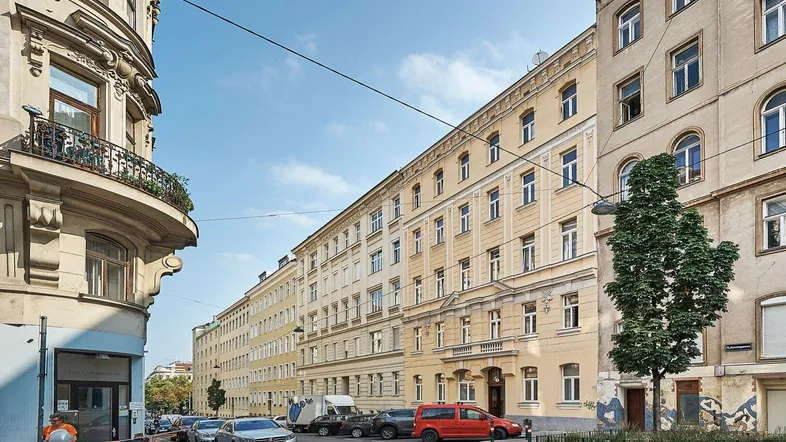 Historisches Wohngebäude in einer städtischen Straße mit geparkten Autos und blauem Himmel.