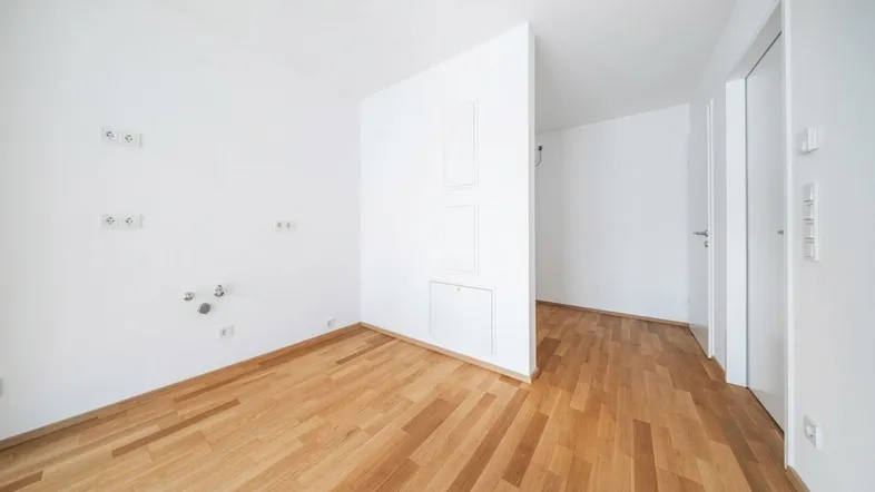 Leerer Raum mit Parkettboden und Anschlüssen für eine Küche, bereit zur individuellen Gestaltung.