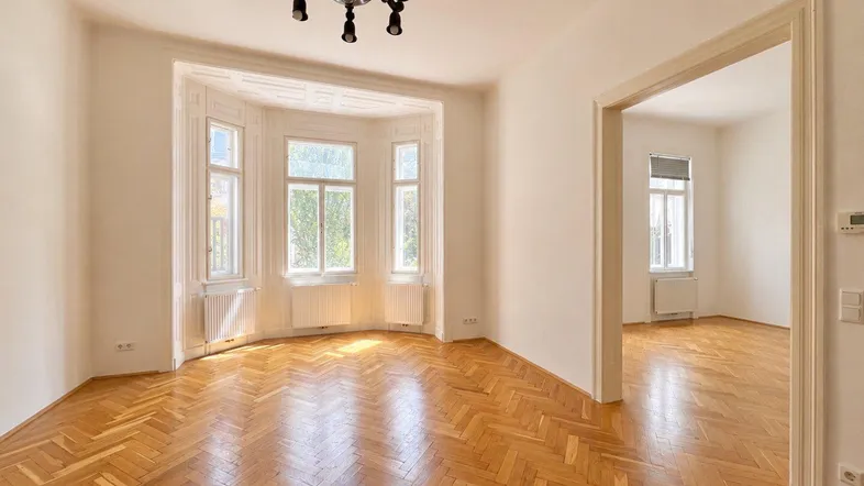 Helles Wohnzimmer mit Fischgrätparkett, Erkerfenstern und hohen Decken, ideal für eine stilvolle Einrichtung.