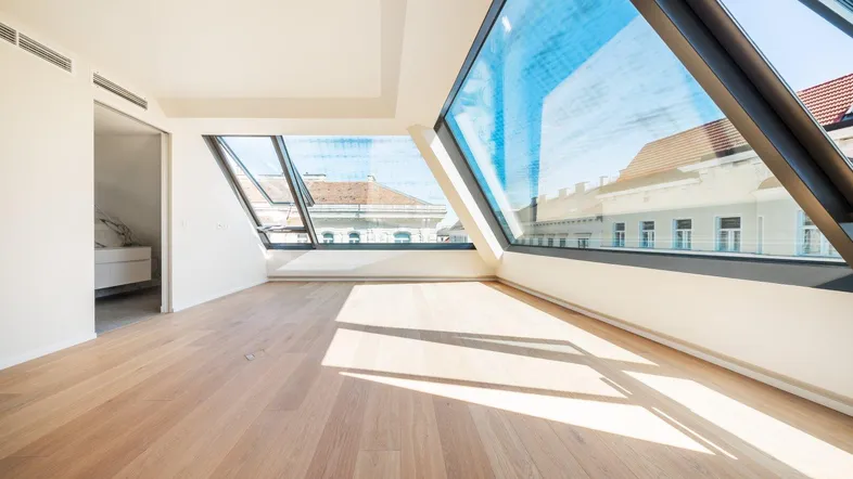 Helles, leeres Zimmer mit großen Dachfenstern und Holzboden, bietet viel natürliches Licht und Stadtblick.