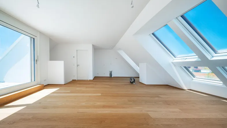 Helles Dachgeschosszimmer mit Holzboden, großen Fenstern und Dachschrägen.