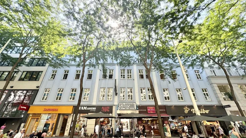 Blick auf die belebte Straße mit Geschäften und Restaurants im Erdgeschoss, umgeben von Bäumen.