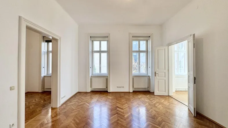 Helles Zimmer mit Fischgrätparkettboden und hohen Fenstern, das viel natürliches Licht hereinlässt.