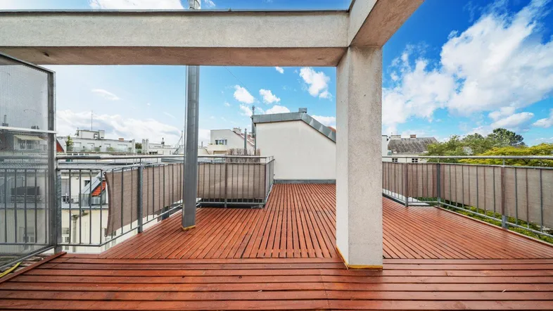 Geräumige Dachterrasse mit Holzboden und Blick auf die umliegenden Gebäude unter blauem Himmel.