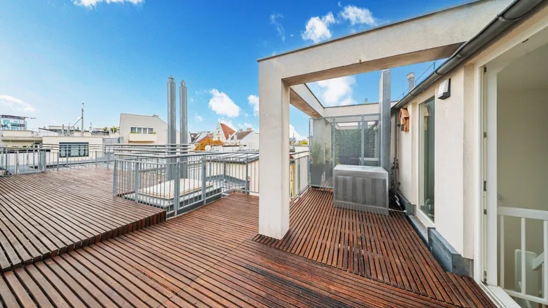 Große Dachterrasse mit Holzbelag und Blick auf die umliegenden Gebäude unter blauem Himmel.