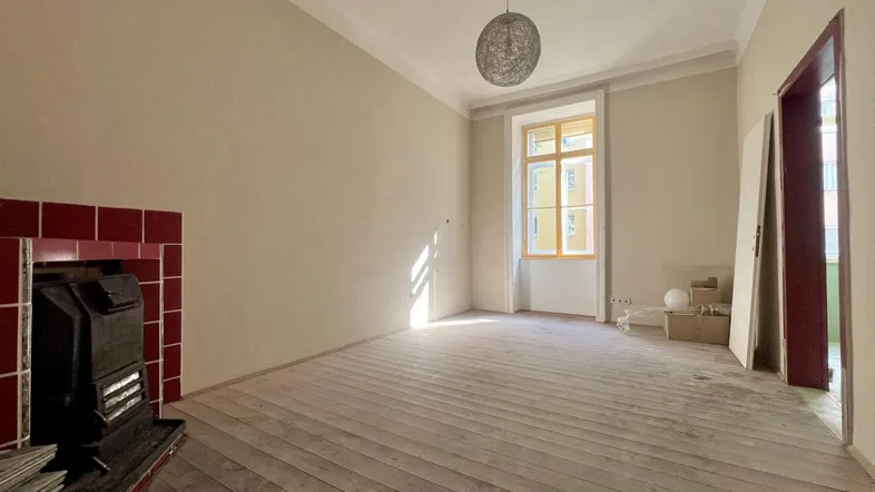 Helles Zimmer mit Holzdielenboden und traditionellem Ofen, bereit für Renovierung.