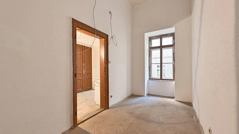 Geräumiger, unrenovierter Raum mit Fischgrätparkett und einem Fenster, das auf den Innenhof blickt.
