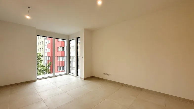 Helles, leeres Zimmer mit großen Fenstern und Zugang zu einem Balkon, ideal als Wohnbereich.