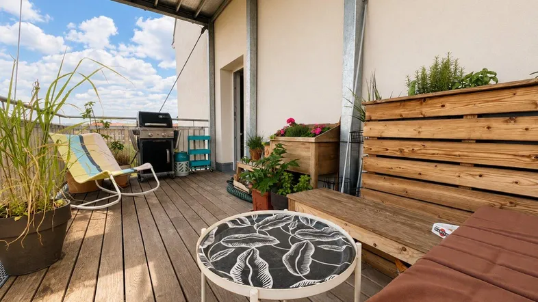 Geräumige Dachterrasse mit Holzdeck, Grillbereich und gemütlichen Sitzgelegenheiten unter blauem Himmel.