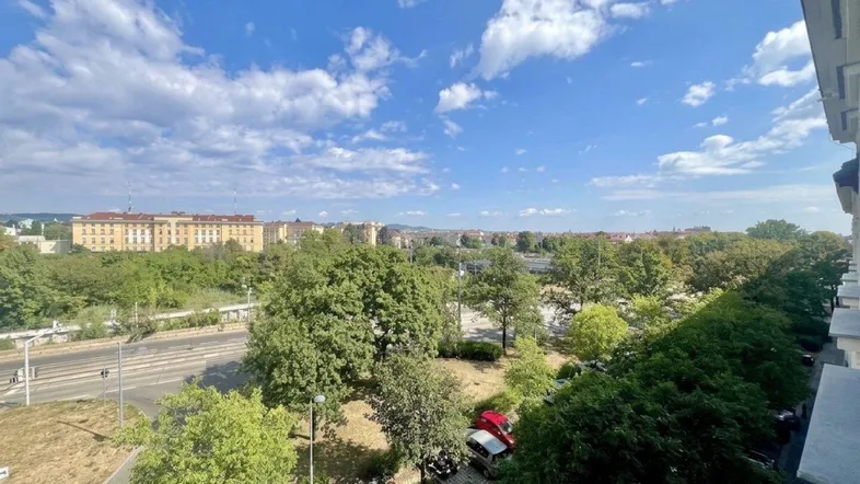 Weitläufiger Blick über die Stadt mit viel Grün und Gebäuden am Horizont unter blauem Himmel.
