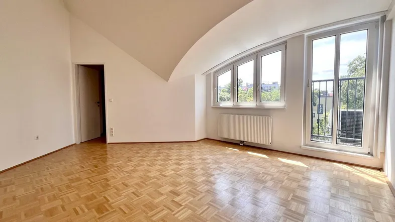 Helles Zimmer im Dachgeschoss mit Parkettboden, schrägen Wänden und Zugang zu einem französischen Balkon.