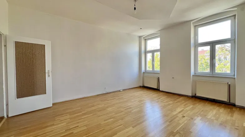 Helles Zimmer mit Parkettboden und zwei Fenstern, bereit zur individuellen Gestaltung.