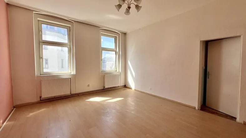 Helles, leeres Zimmer mit Parkettboden und zwei Fenstern, bereit zur individuellen Gestaltung.