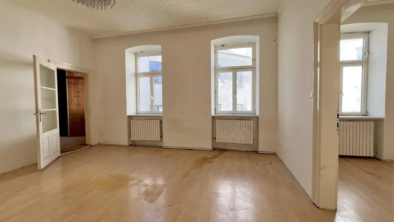Geräumiges Wohnzimmer mit Parkettboden, hohen Decken und zwei Fenstern, bereit zur Renovierung.