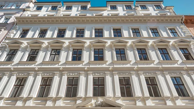 Elegante weiße Fassade eines historischen Gebäudes mit vielen Fenstern und Zierelementen.
