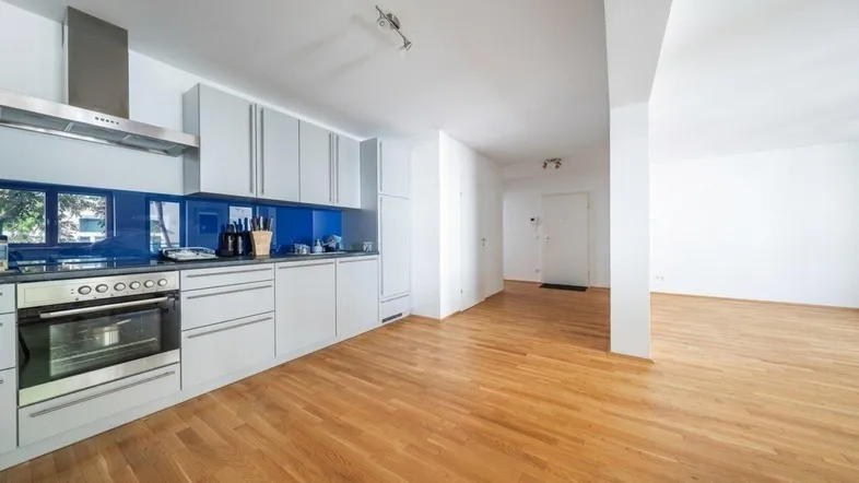 Moderne Einbauküche mit blauer Rückwand und Holzfußboden, offen zum Wohnbereich.