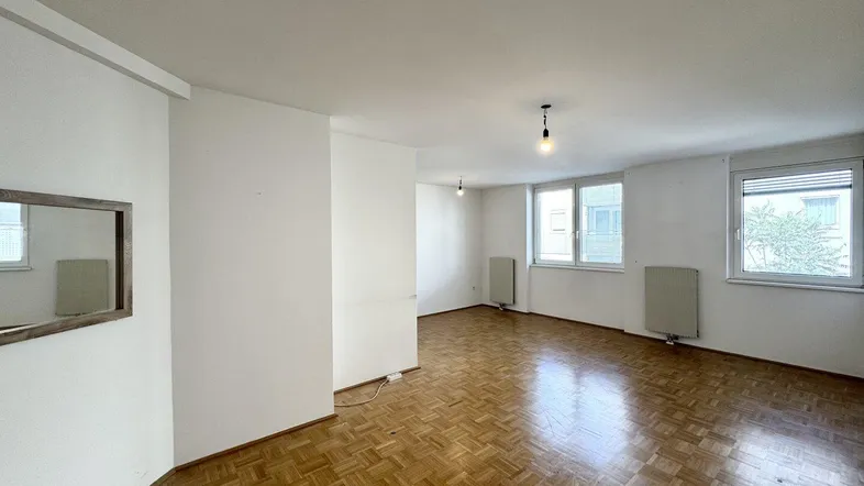 Helles, leeres Wohnzimmer mit Parkettboden und mehreren Fenstern, bereit zur individuellen Gestaltung.
