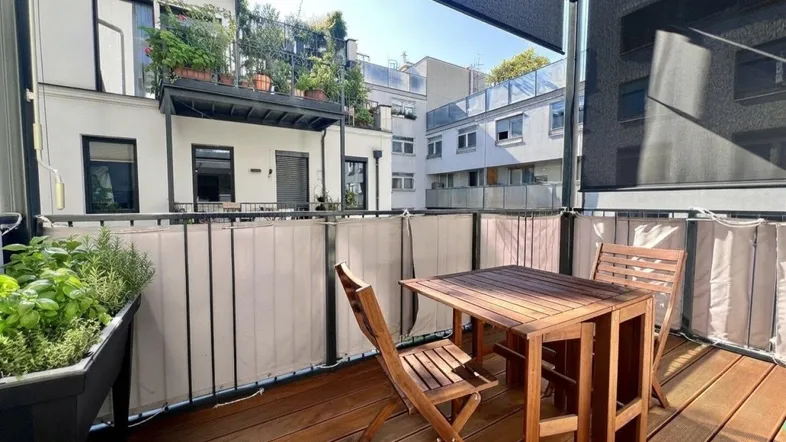 Gemütlicher Balkon mit Holzboden, Sitzgelegenheiten und Blick auf den Innenhof.