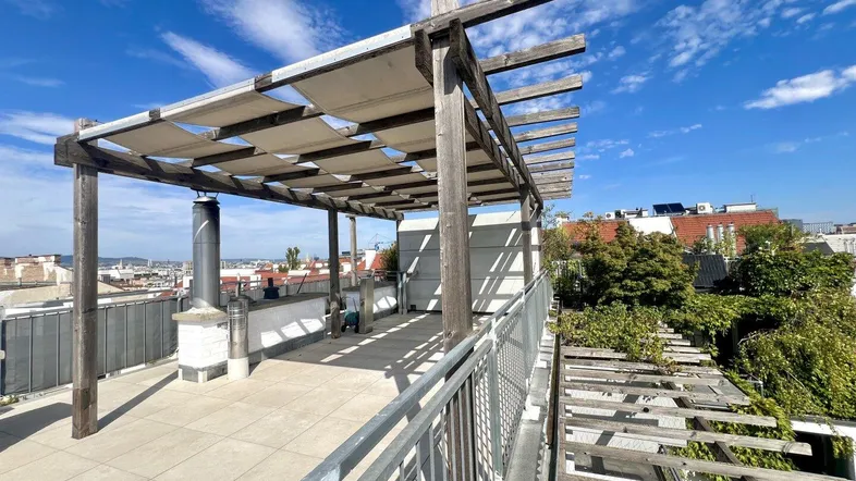 Große Dachterrasse mit Holzpergola, Fliesenboden und weitem Blick über die Stadt.